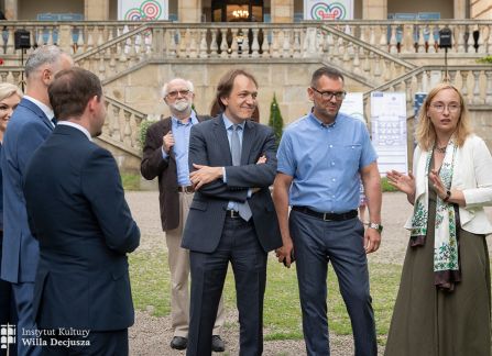 fotografia. art piknik w willi decjusza. dyrektorka instytutu kultury willa decjusza dominika kasprowicz wraz z grupą gości stoją na placu przed willą, w tle fasada budynku.